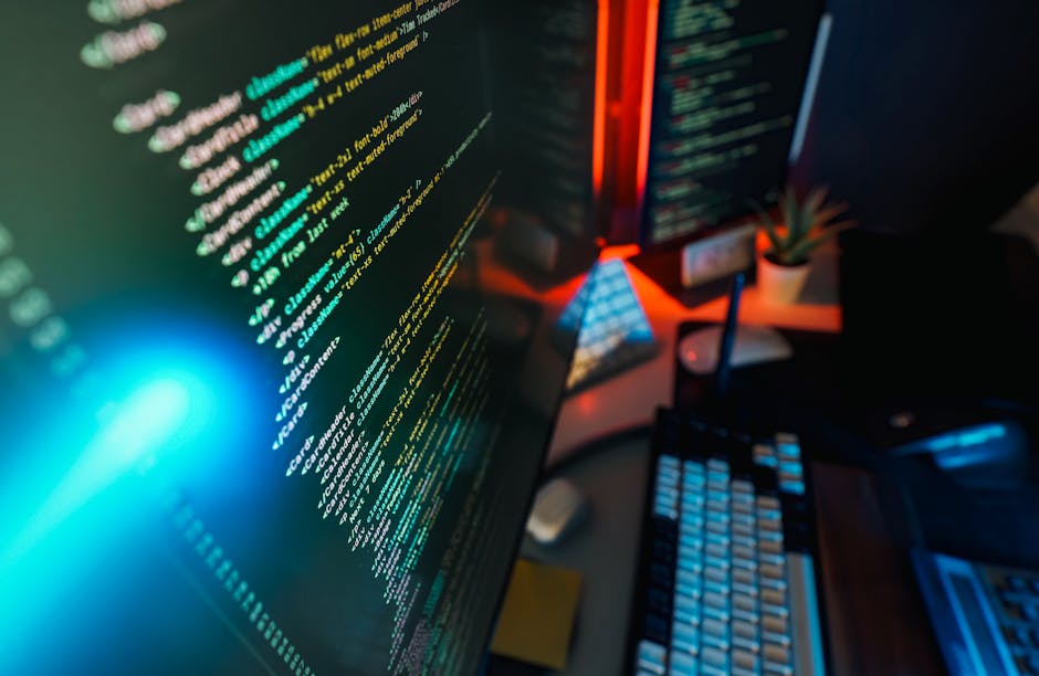 A close-up view of a computer monitor displaying lines of colorful code on a dark background, with a brightly glowing blue light source illuminating part of the screen. The monitor is situated on a cl